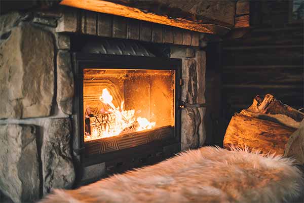 Chimney service Lacey keeps fireplaces safe; fire burning in stone fireplace with cord of wood and fluffy white rug in front of fireplace