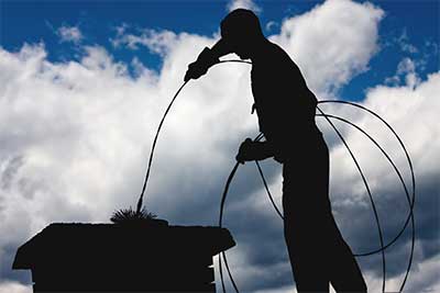 Chimney service Lacey expert in silhouette with brush in top of chimney